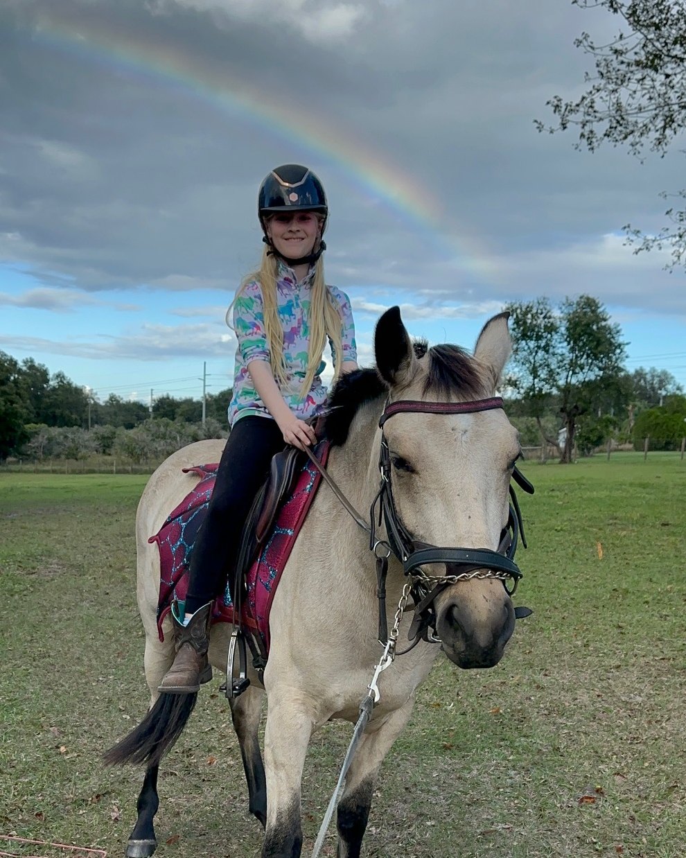 Coletta sitting on Zenni for the first time, with a rainbow in the sky behind them
