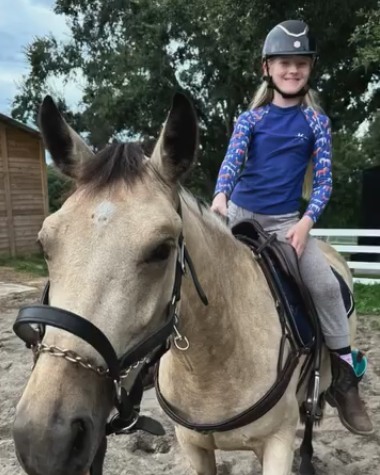 A small girl in a helmet sitting on Zenni, a buckskin pony, for her first ride